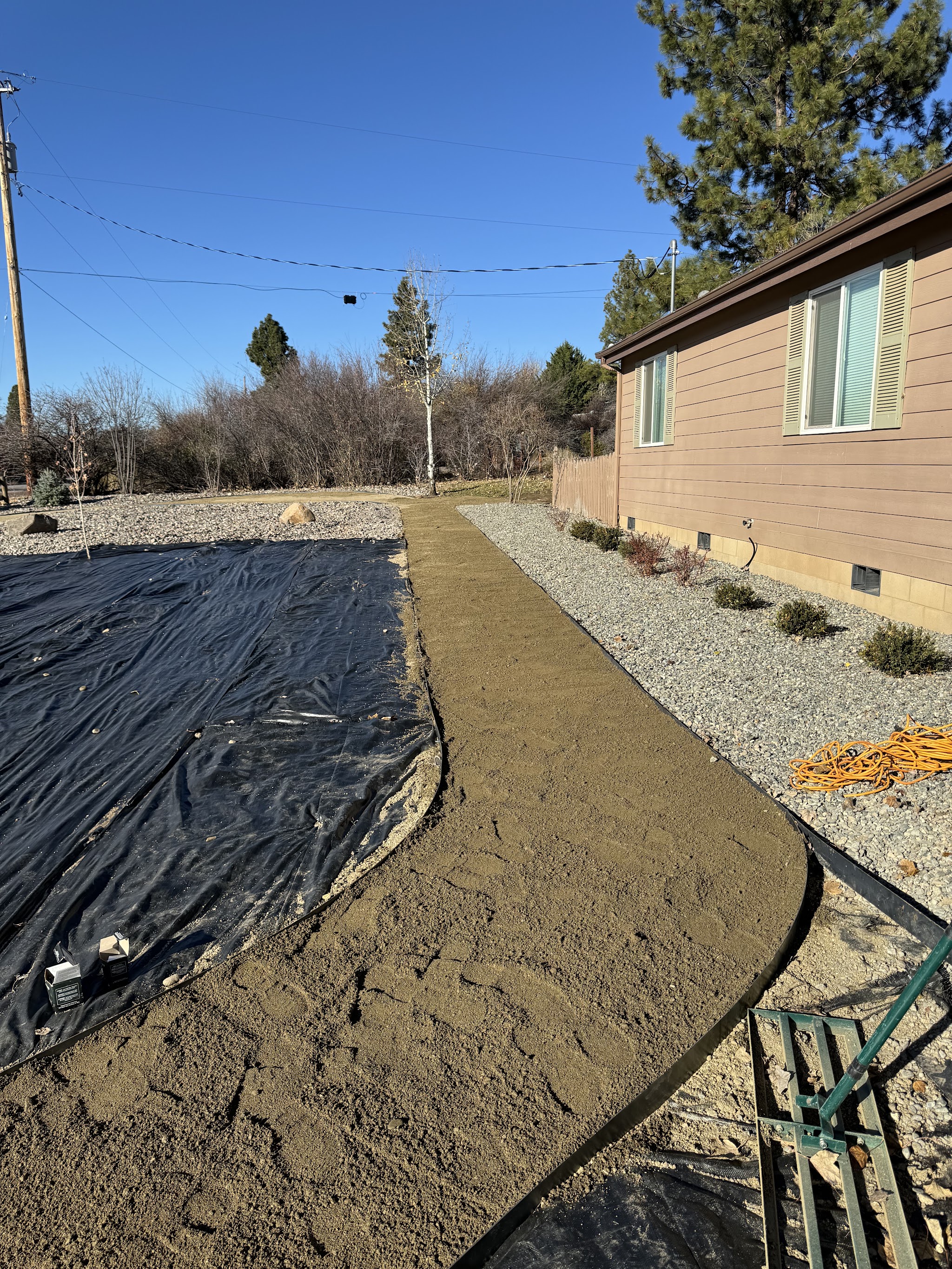 Freshly poured concrete walkway curving through a backyard, edged in river rock