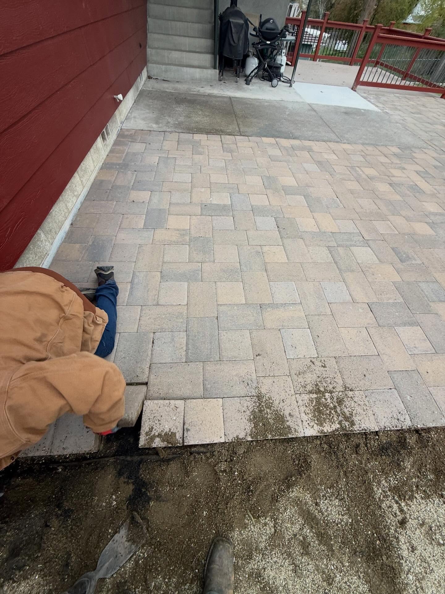 Paver patio installation in progress alongside a home